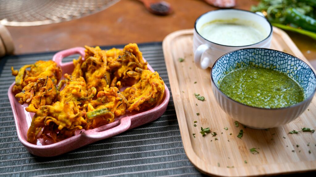 Delicious Indian pakora served with green chutney on a wooden tray.